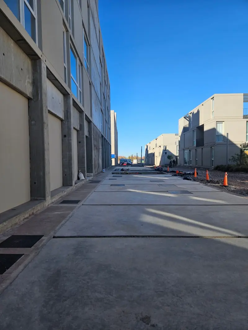 Finished concrete sidewalk between buildings, with site traffic cones