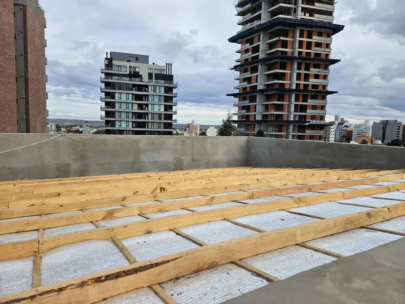 Azotea con listones de madera apoyados sobre la aislación y edificios en altura al fondo