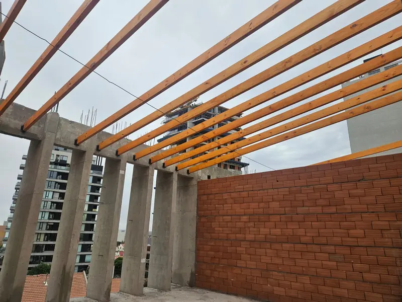Vigas de madera del techo apoyadas sobre columnas de hormigón junto a muro de ladrillo visto
