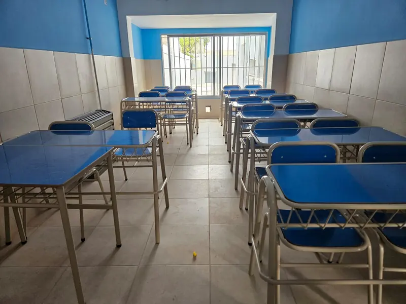 Aula terminada y equipada con bancos y sillas, piso cerámico y ventanal con reja