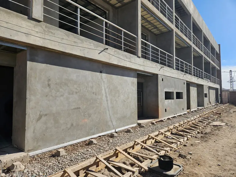 Ground floor concrete walls and first-floor balconies, with materials stored on the sidewalk