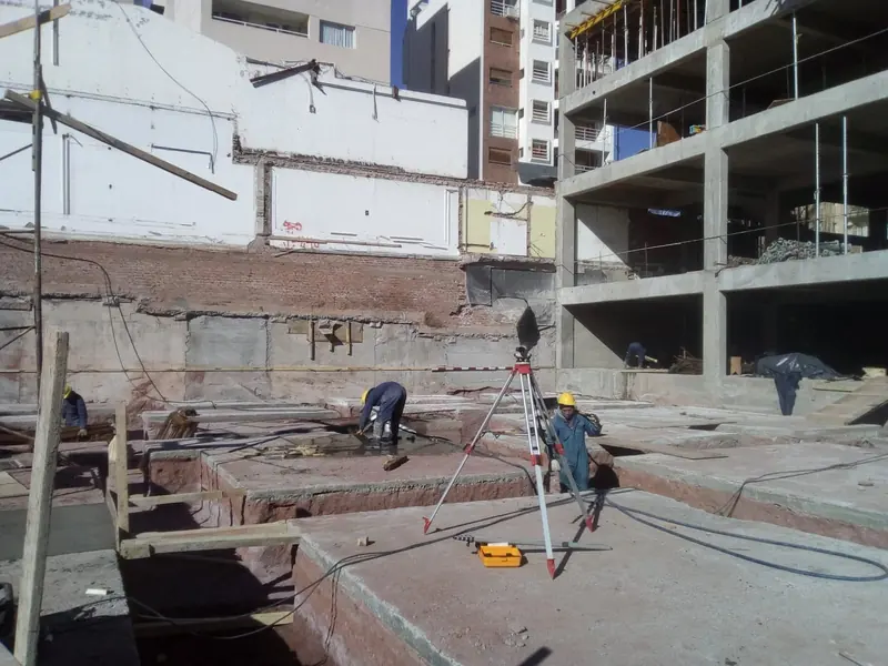 Worker with an optical level setting out the site in front of the concrete structure