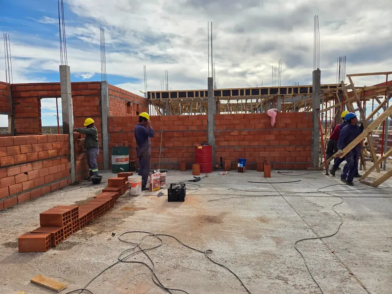 Operarios levantando muros de ladrillo cerámico sobre losa de hormigón, con columnas ya armadas