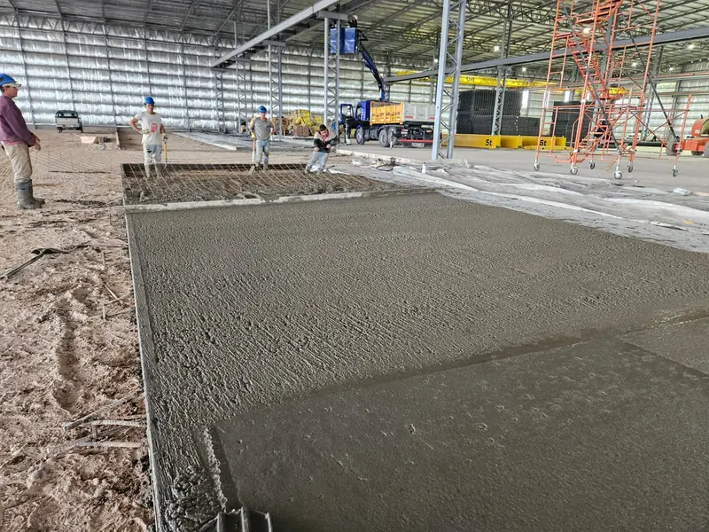 Crew pouring and floating the industrial floor slab inside the steel-framed shed