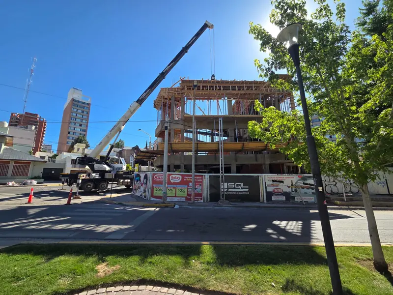 The building at the structural stage seen from across the street, with a truck-mounted crane and site hoarding