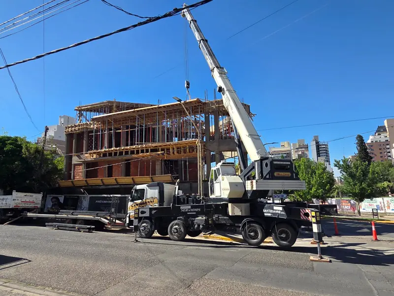 Truck-mounted crane lifting material in front of the building at the structural stage