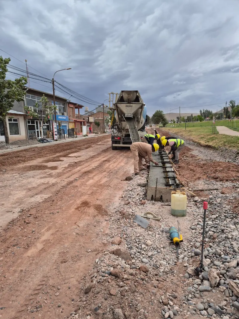 Crew pouring curb and gutter from a concrete mixer truck on a street in Añelo