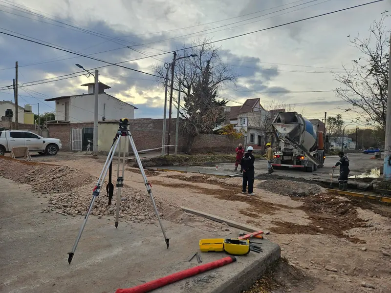 Optical level on a tripod and crew pouring a curb as the mixer truck discharges