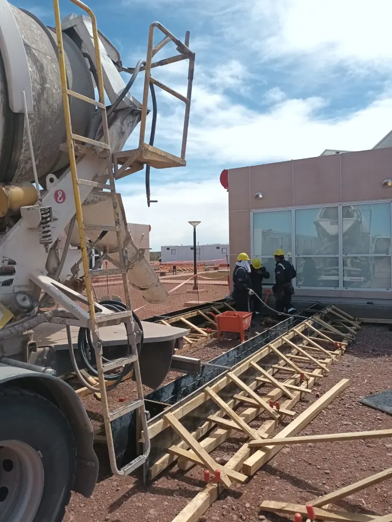 Self-loading mixer discharging concrete into the formwork with workers in hard hats and hi-vis vests
