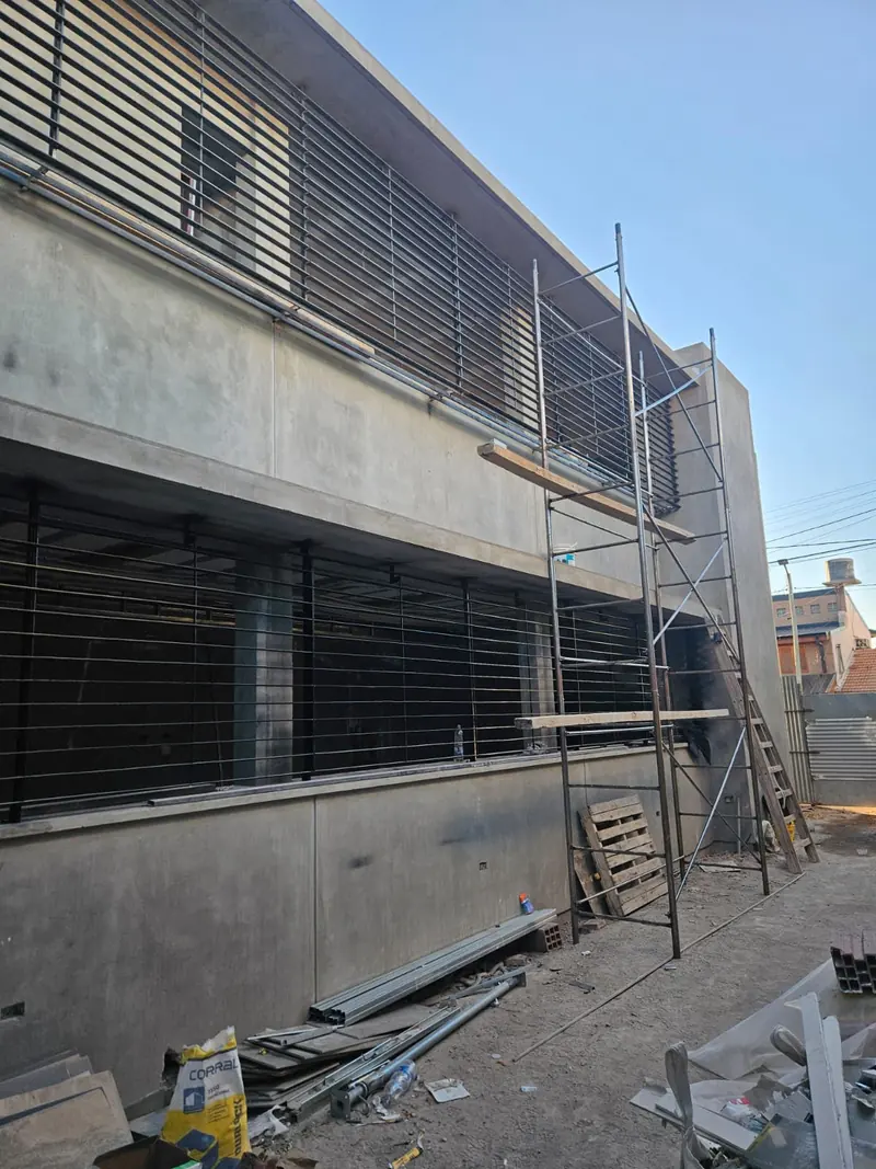 Exposed concrete facade with metal sun louvres and scaffolding during the works