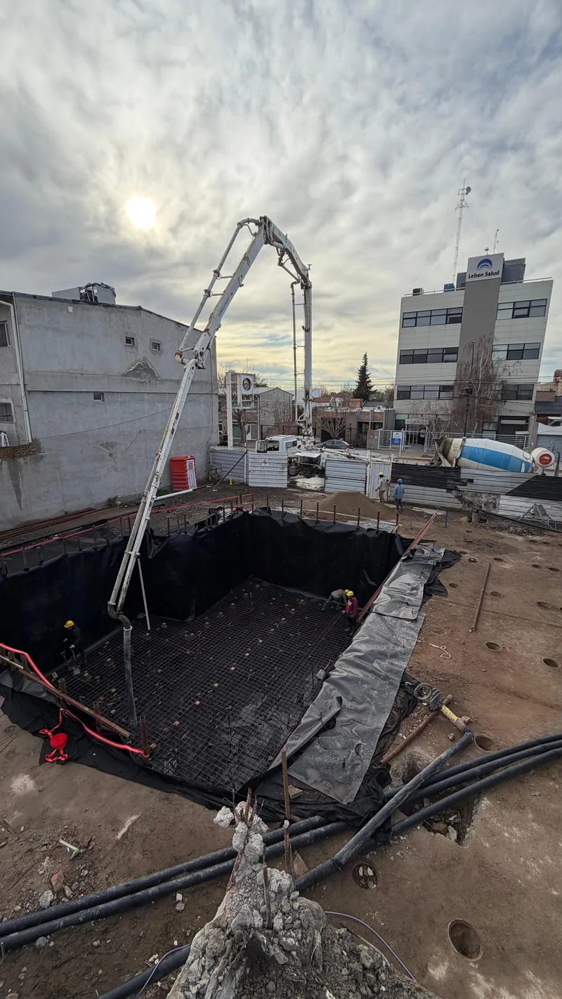 Bomba pluma hormigonando junto a la excavacion, edificios linderos de fondo