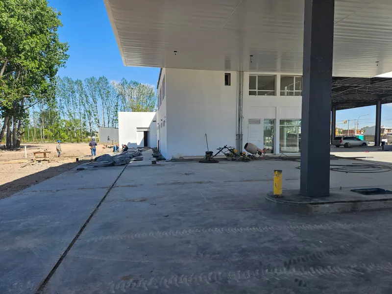 Playa de despacho con techo blanco terminado y edificio de la estación en etapa final de obra