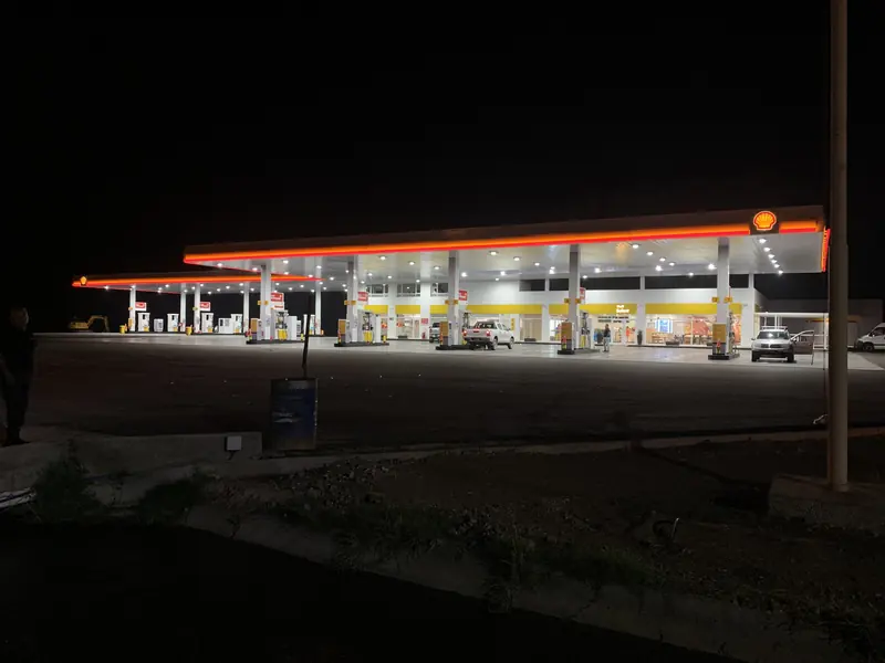 Estación de servicio Shell iluminada de noche, con la playa de despacho en funcionamiento