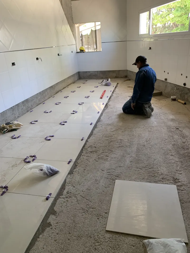 Operario colocando porcelanato con crucetas niveladoras en el local en obra