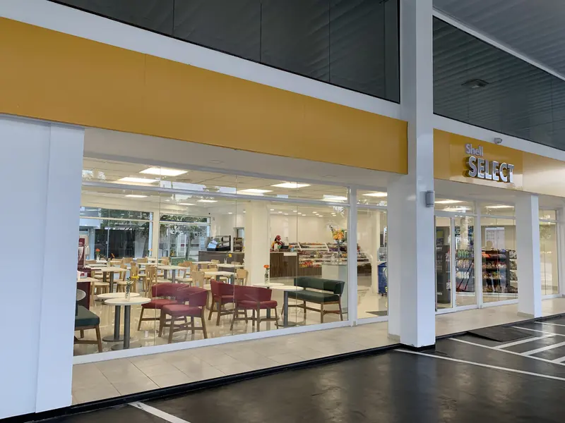 Frente vidriado de la tienda Shell Select terminada, con mesas y sillas