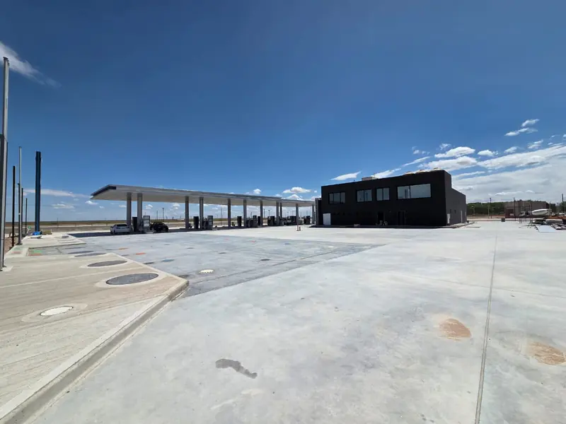 Finished concrete forecourt with white canopy and dark-fronted shop building