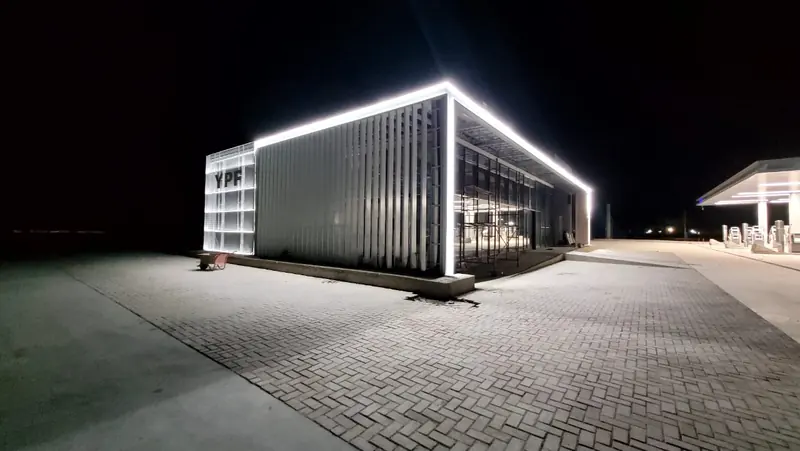 Station shop lit at night with perimeter strip lighting and block paving